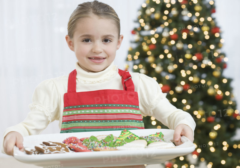 Girl carrying tray of Christmas cookies.