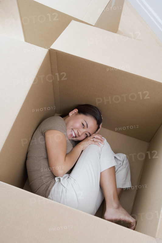 Woman curled up in empty moving box.