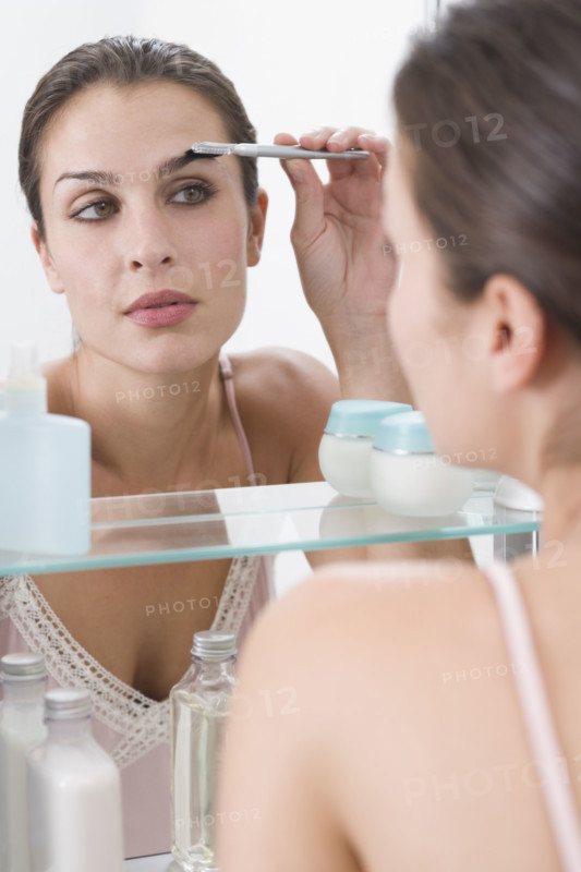 Woman combing eyebrows in mirror.