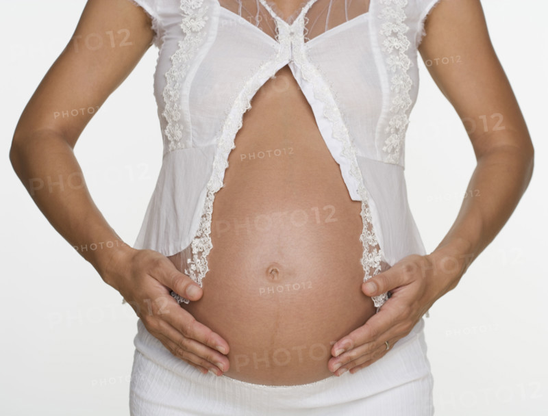 Close up of pregnant woman with hands on stomach.