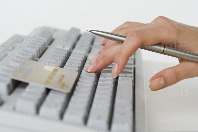 Close up of woman's hand holding pen with credit card and computer keyboard.