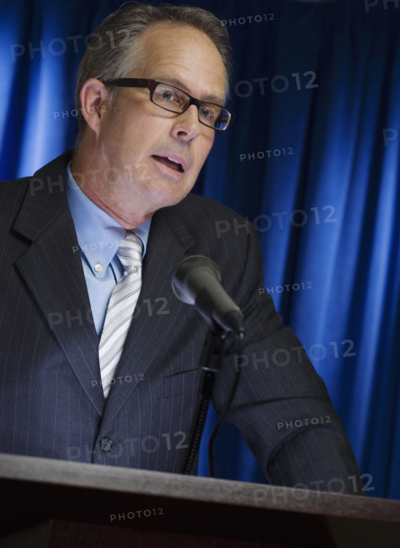 Close up of businessman speaking at podium.