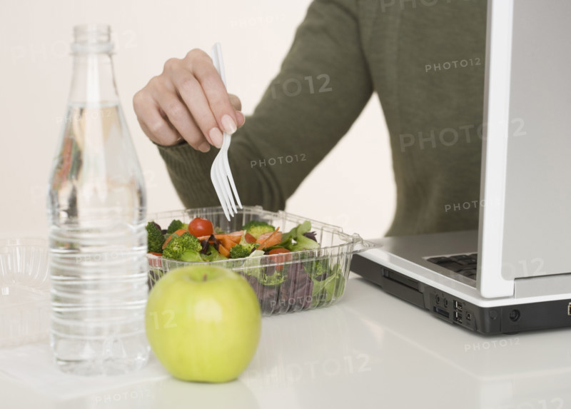 Woman eating salad next to laptop.