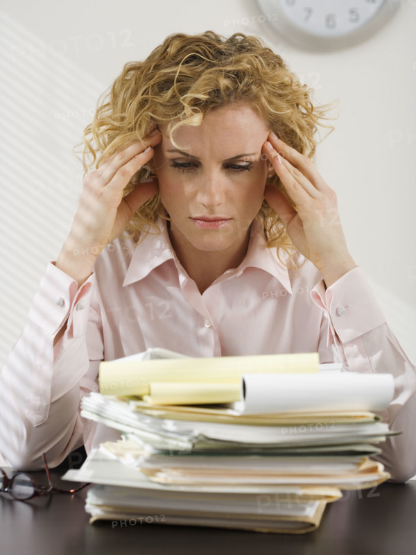 Businesswoman rubbing temples and looking at paperwork.