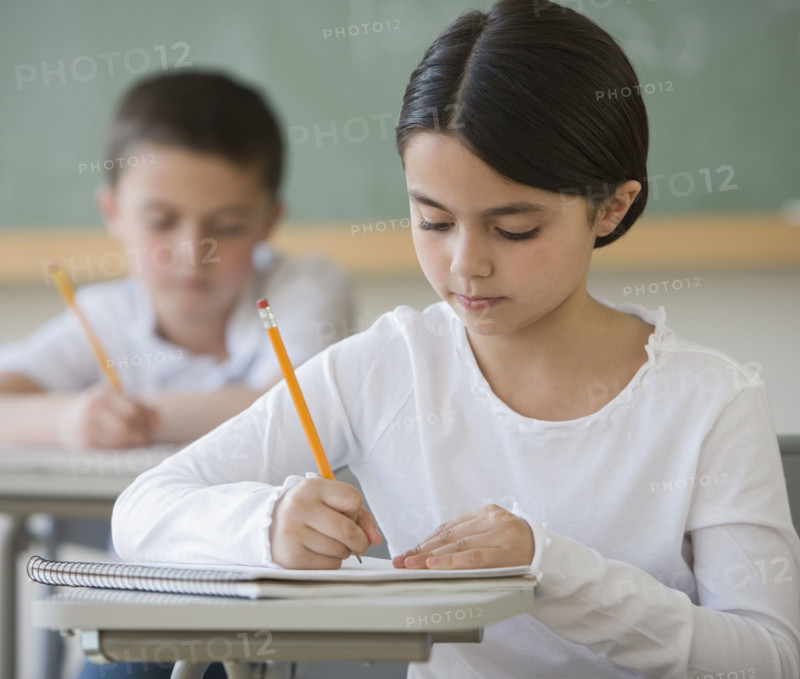 Girl writing at desk in classroom.