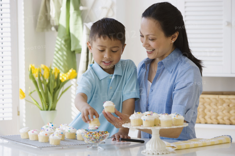 Asian mother and son decorating cupcakes.
