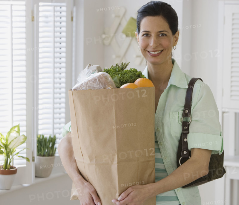 Woman holding bag of groceries in kitchen.