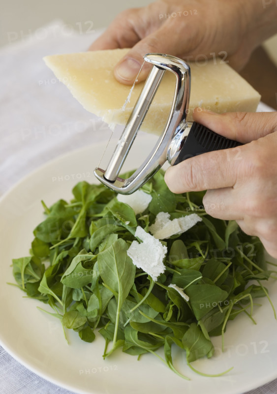 Man shaving cheese onto salad.
