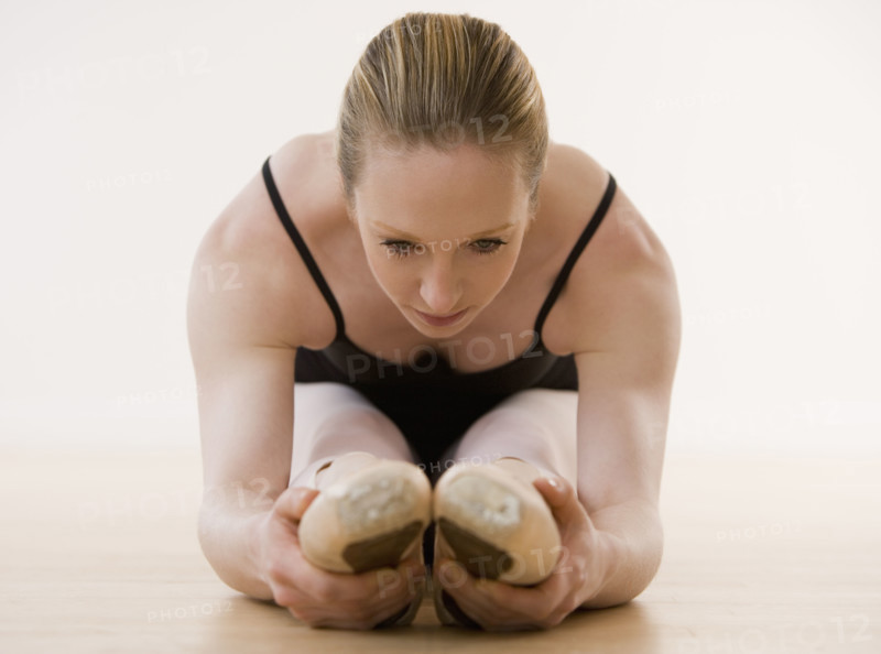 Female ballet dancer stretching on floor.