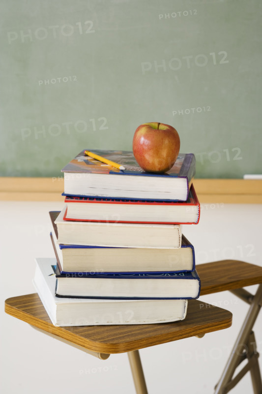 Stack of books and apple in classroom.