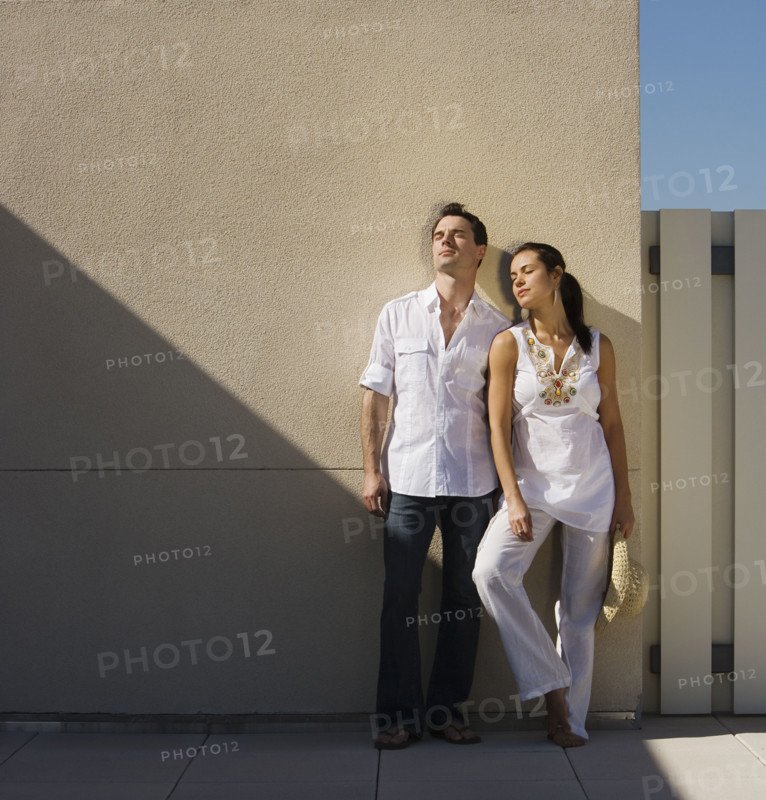 Woman leaning on wall in sunlight.