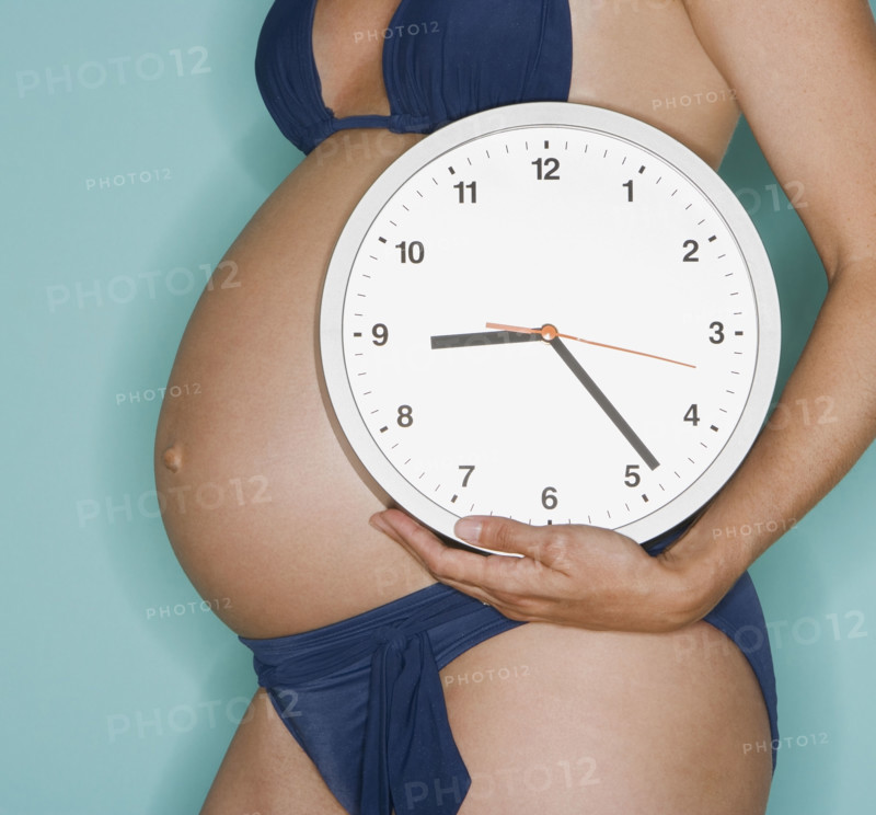 Pregnant woman holding wall clock.