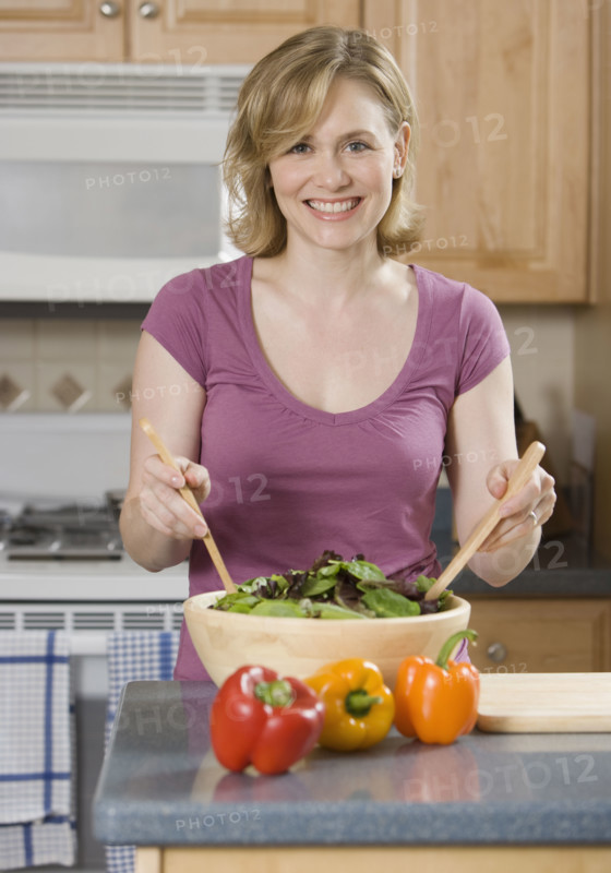 Woman tossing salad in kitchen.