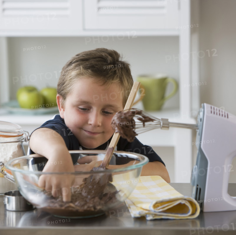 Boy sticking finger into bowl of batter.