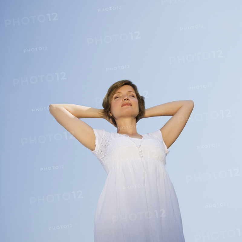 Low angle view of woman with arms behind head.