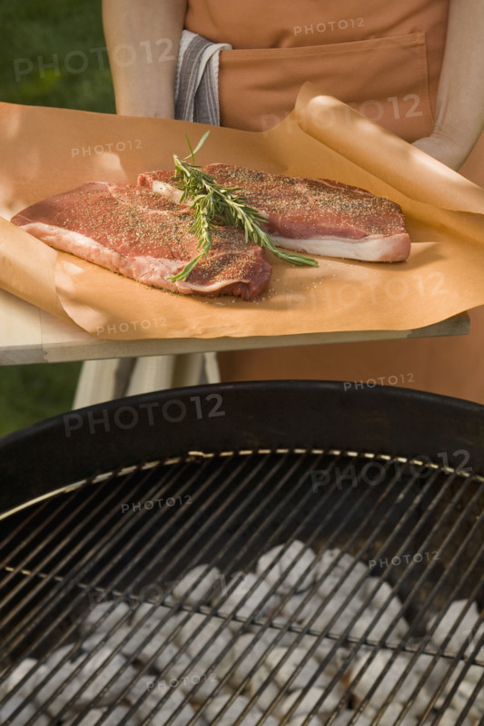 Person holding steaks next to grill.