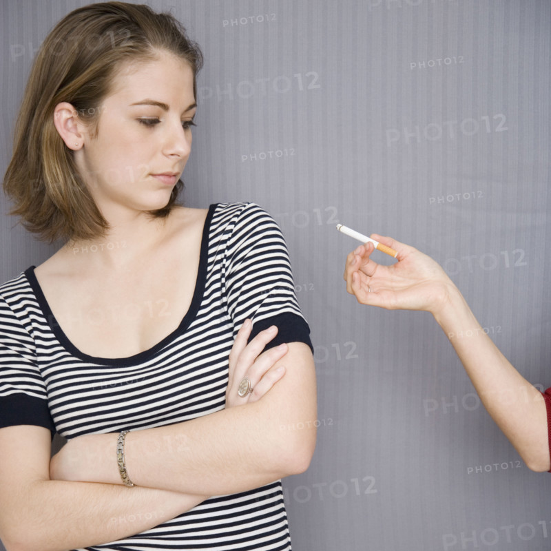 Teenage girl looking at cigarette in friend’s hand. Date : 2007