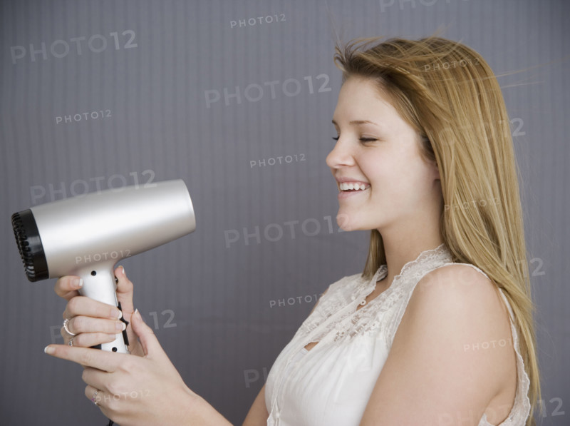 Teenage girl pointing hair dryer at face. Date : 2007