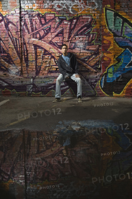 Asian man sitting in front of graffitied wall. Date : 2007