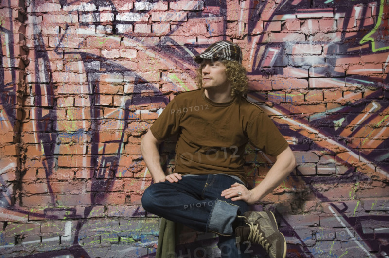 Young man sitting in front of graffitied wall. Date : 2007
