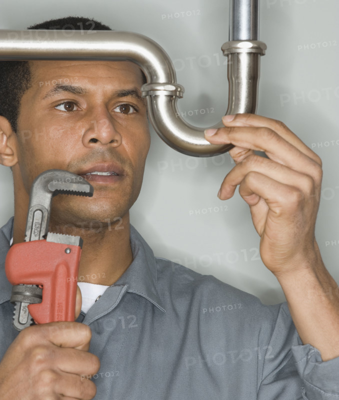 African male plumber holding wrench next to pipe.