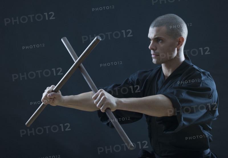 Hispanic male holding sticks in fighting stance.