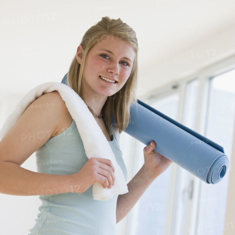 Teenaged girl holding rolled yoga mat.