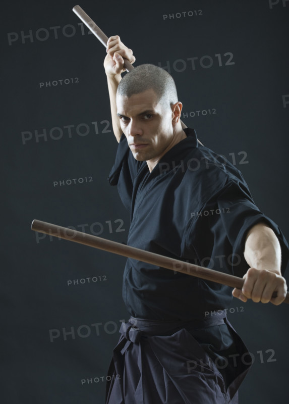 Hispanic male holding sticks in fighting stance.