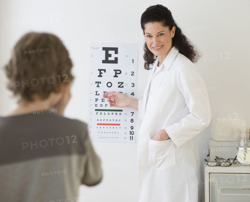 Hispanic female doctor pointing at eye chart for child.