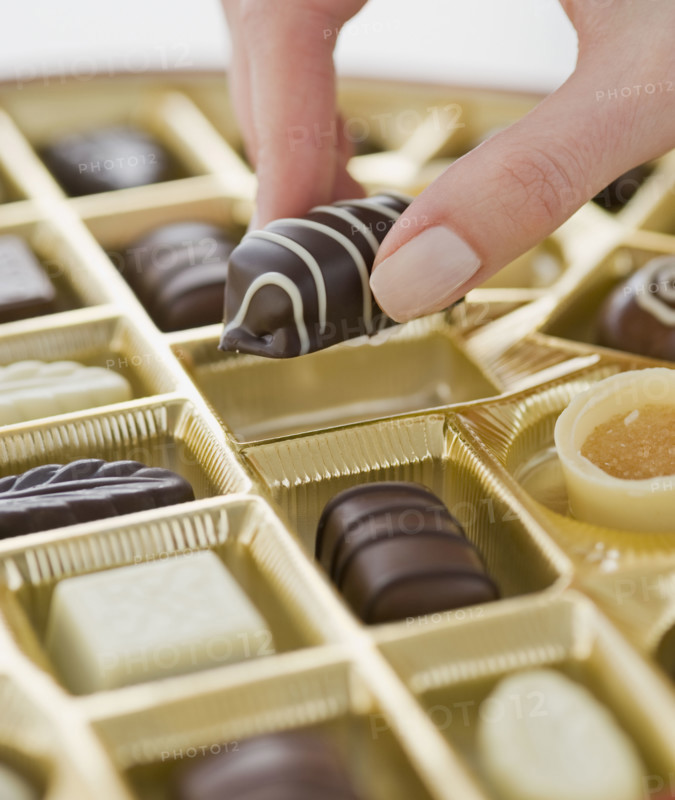 Woman holding chocolate over box of chocolates.