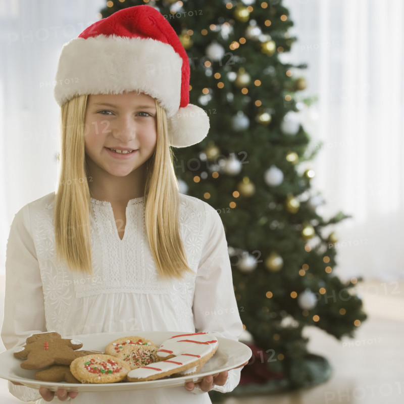 Girl in Santa Claus hat holding plate of cookies.