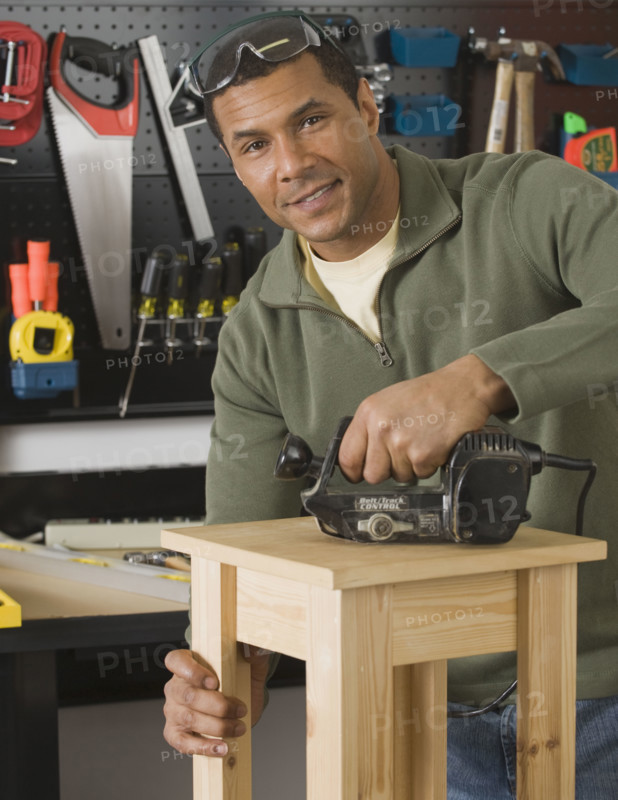 African male woodworker sanding table.