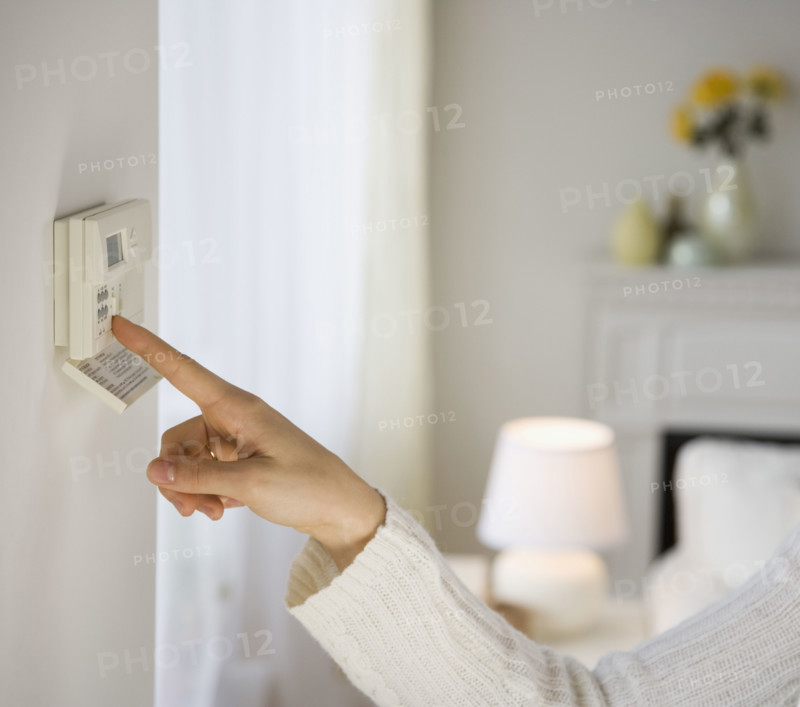 Woman adjusting digital thermostat.