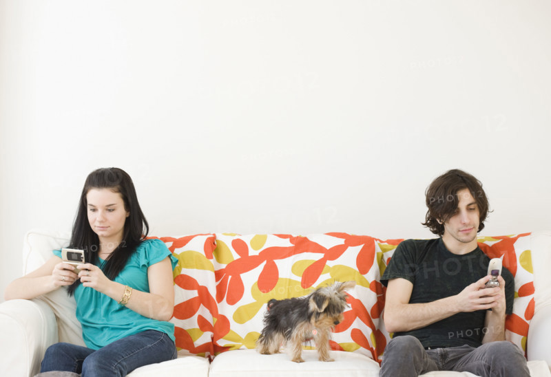 Man and woman dialing cell phones on opposite ends of sofa. Date : 2008