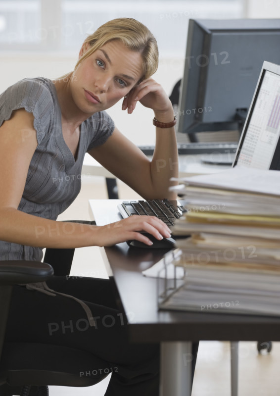 Businesswoman with stack of paperwork on desk.