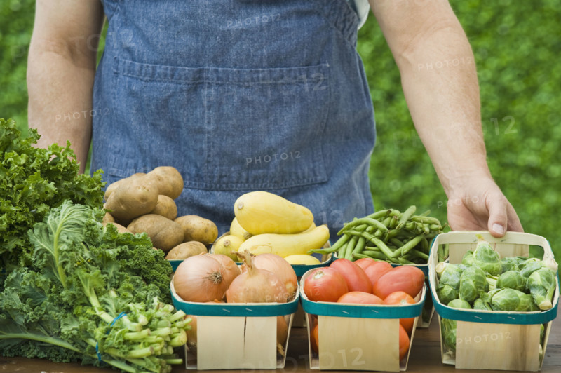 Farmer next to baskets of vegetables.