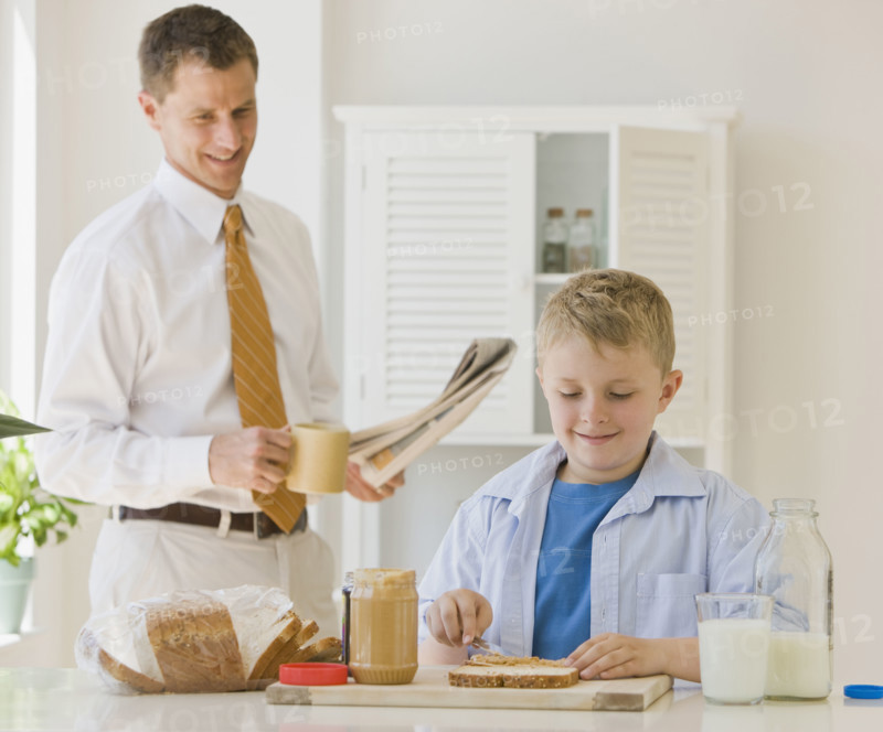 Father watching son make sandwich.