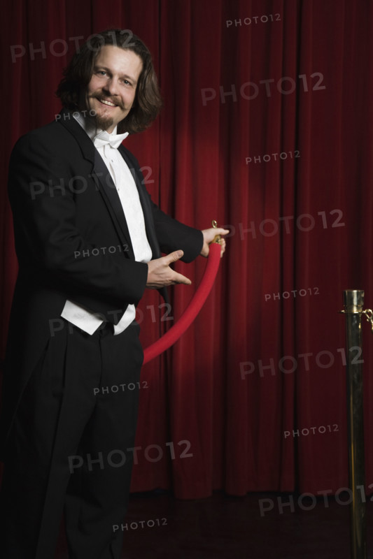Man in tuxedo holding velvet rope. Date : 2008