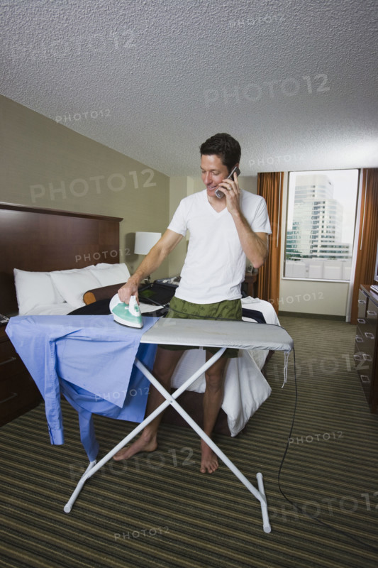 Businessman ironing shirt and talking on cell phone. Date : 2008