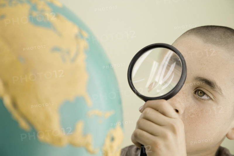 Boy examining globe with magnifying glass. Date : 2008