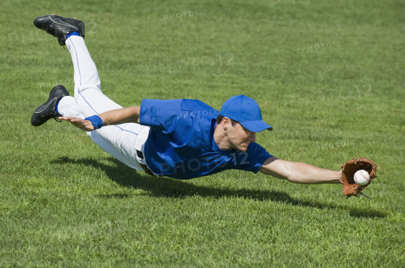 Baseball player diving to catch baseball.
