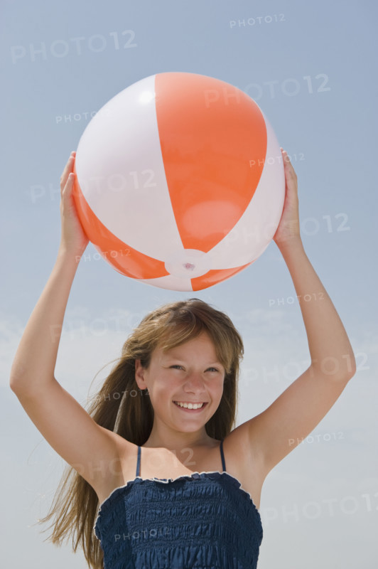 Girl holding beach ball above head.