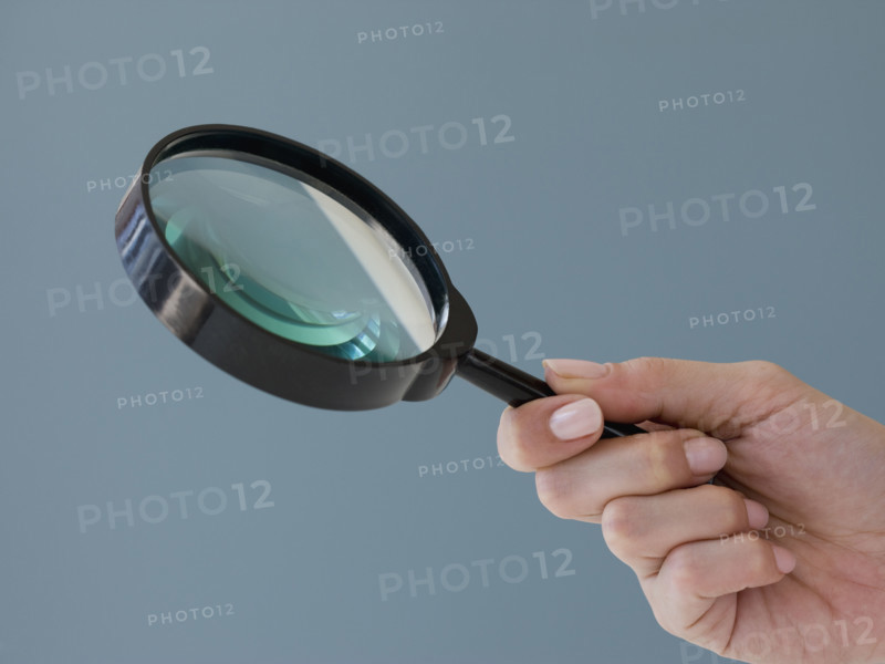 Close up of hand holding magnifying glass.