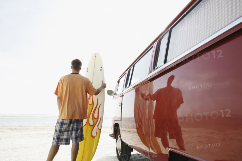 Man holding surfboard next to van on beach. Date : 2008