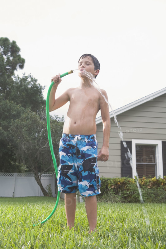 Boy drinking from garden hose in backyard. Date : 2008