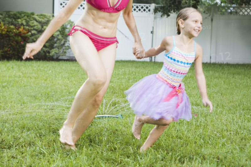 Mother and daughter running through sprinkler. Date : 2008