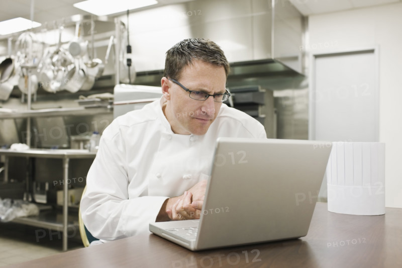 Frustrated chef looking at laptop in kitchen. Date : 2008