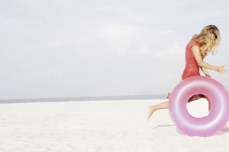 Teenage girl rolling inflatable ring on beach. Date : 2008