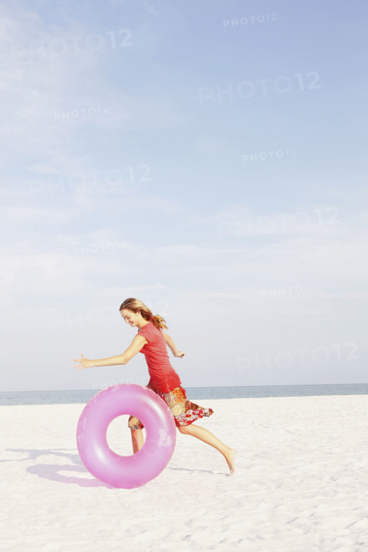 Teenage girl rolling inflatable ring on beach. Date : 2008