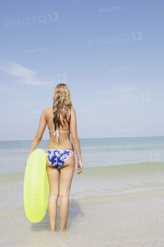 Teenage girl holding inflatable ring contemplating ocean waves. Date : 2008